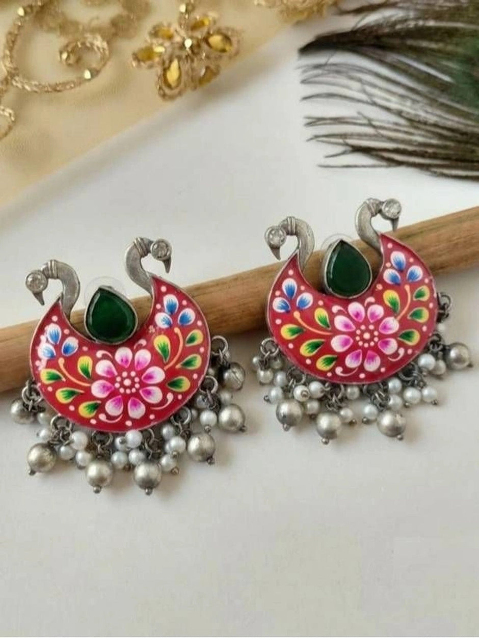 Pair of red meenakari chandbali earrings displayed on wooden prop with peacock feather