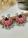 Pair of red meenakari chandbali earrings displayed on wooden prop with peacock feather