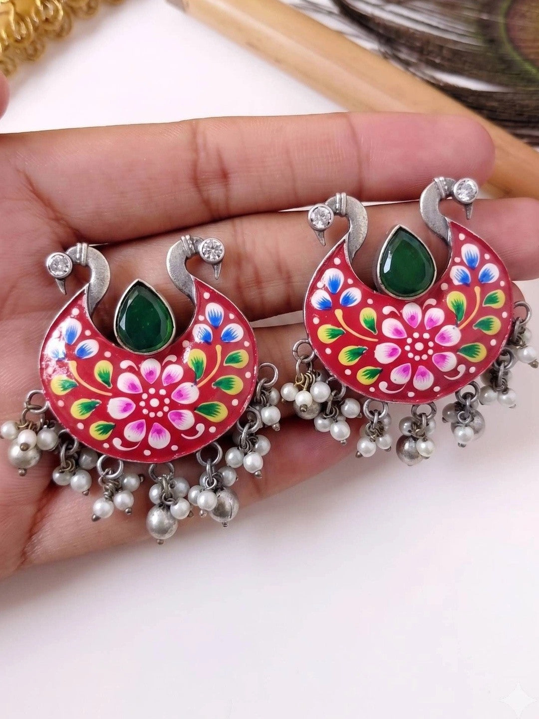 Both red meenakari chandbali earrings held in hand showing pearl bead fringe detail