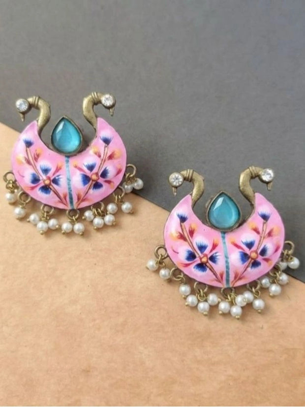 Pair of pink meenakari chandbali earrings laid flat on grey and beige surface