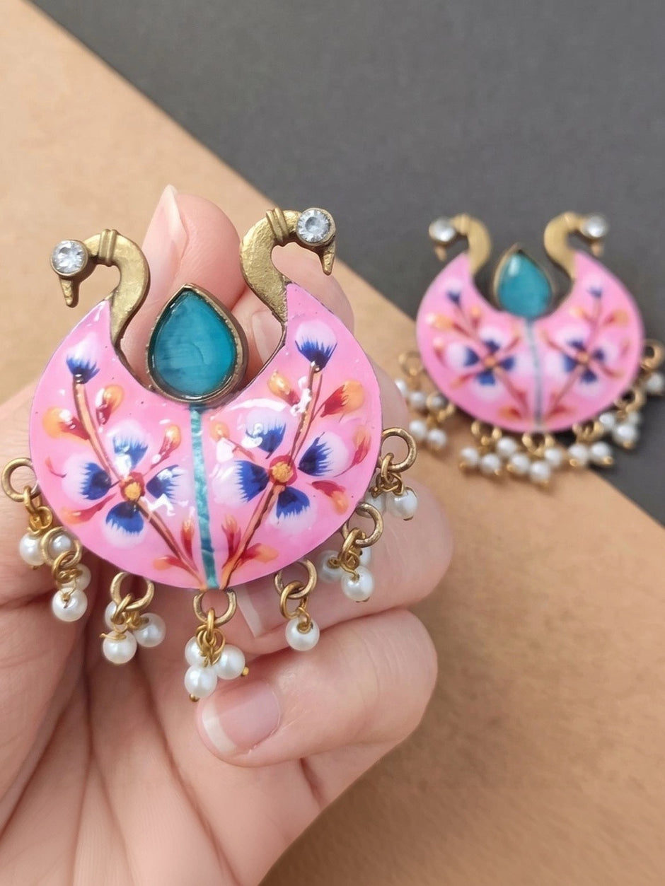 Hand holding pink meenakari chandbali earring close up with second earring in background