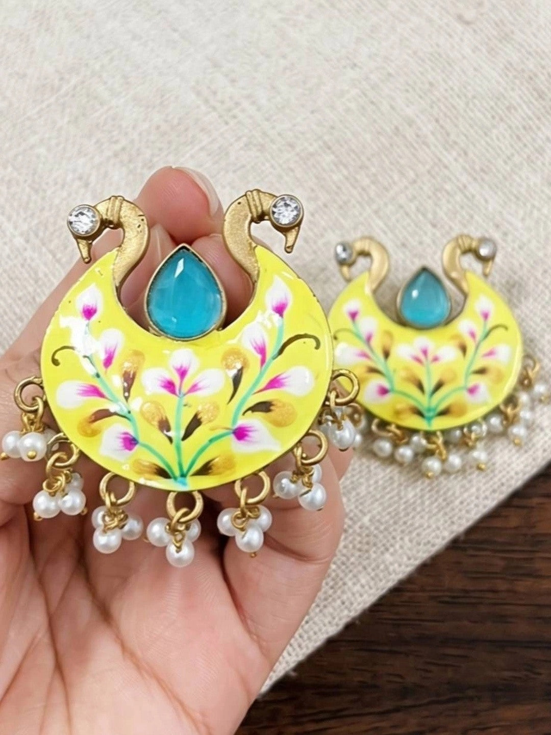 Close-up of meenakari chandbali earrings held in hand showing floral enamel detail and pearl drops