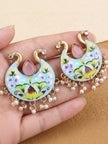 Pair of sky-blue meenakari peacock chandbali earrings with pearl drops held on a palm