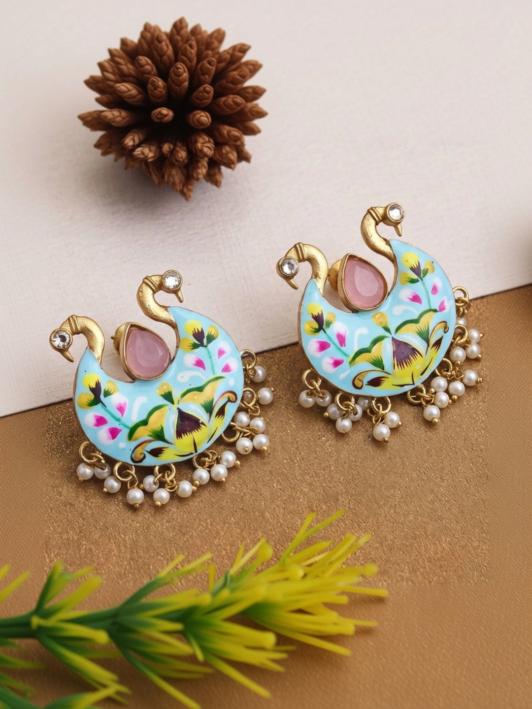 Both meenakari peacock chandbali earrings displayed flat on a gold surface
