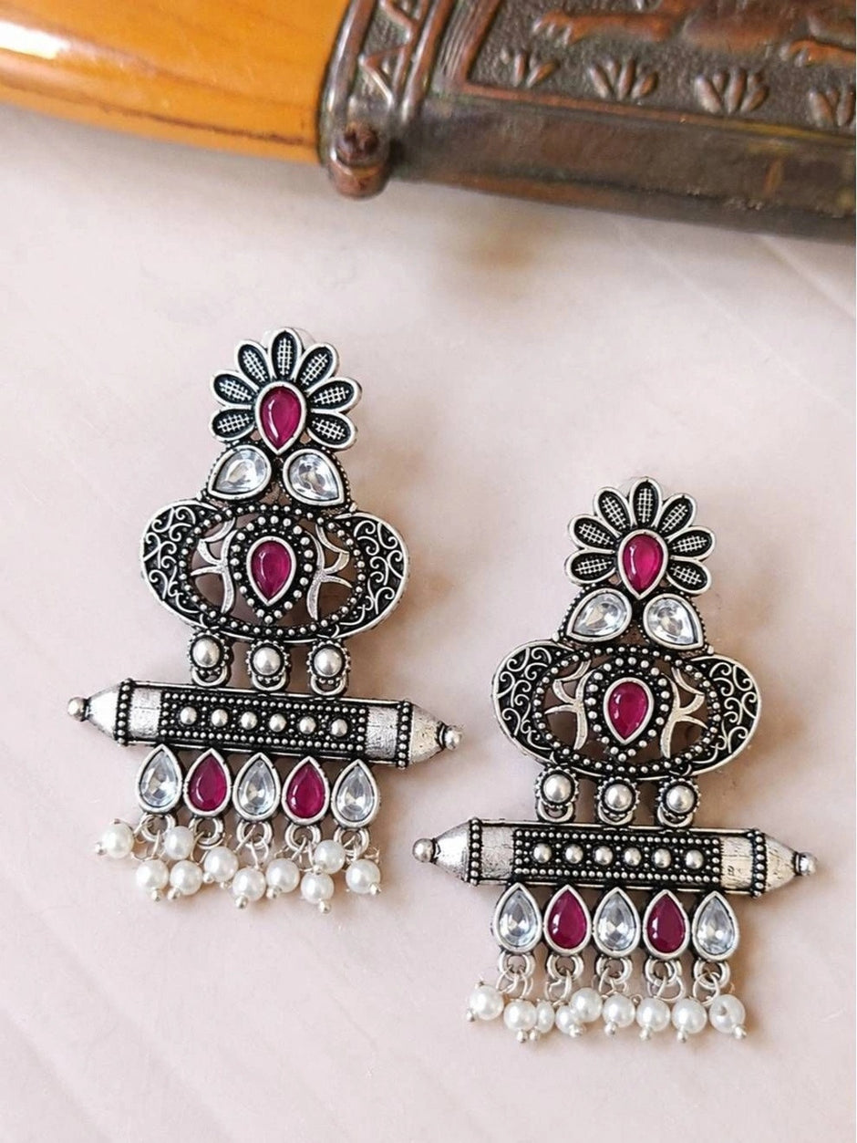 Pair of oxidised silver chandbali earrings with red and clear teardrop stones and pearl drops on white surface