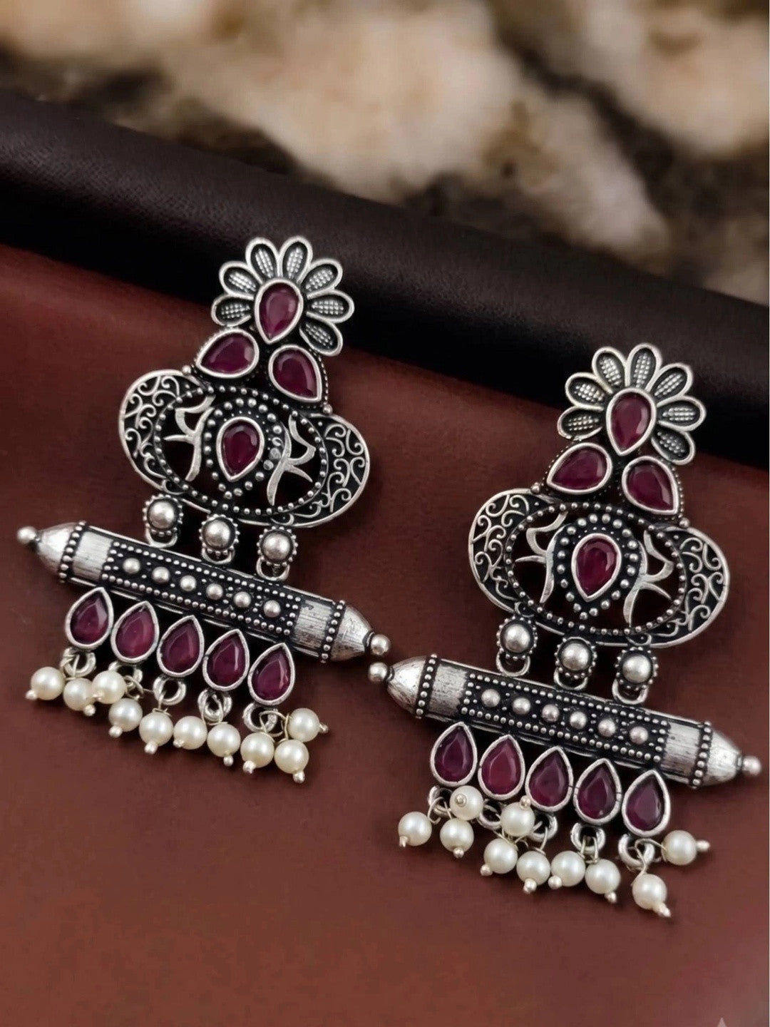 Pair of oxidised silver chandbali earrings with red teardrop stones laid flat on dark surface