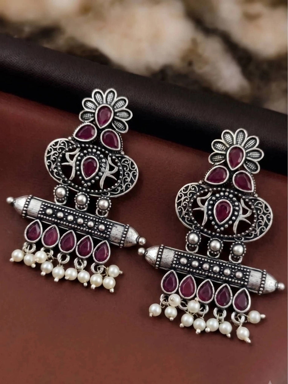 Pair of oxidised silver chandbali earrings with red teardrop stones laid flat on dark surface