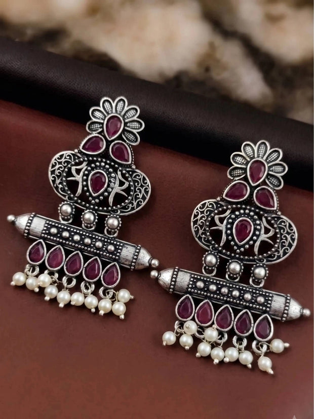 Pair of oxidised silver chandbali earrings with red teardrop stones laid flat on dark surface