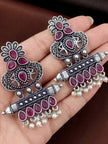 Pair of oxidised silver chandbali earrings with ruby stones and pearl drops held in open palm