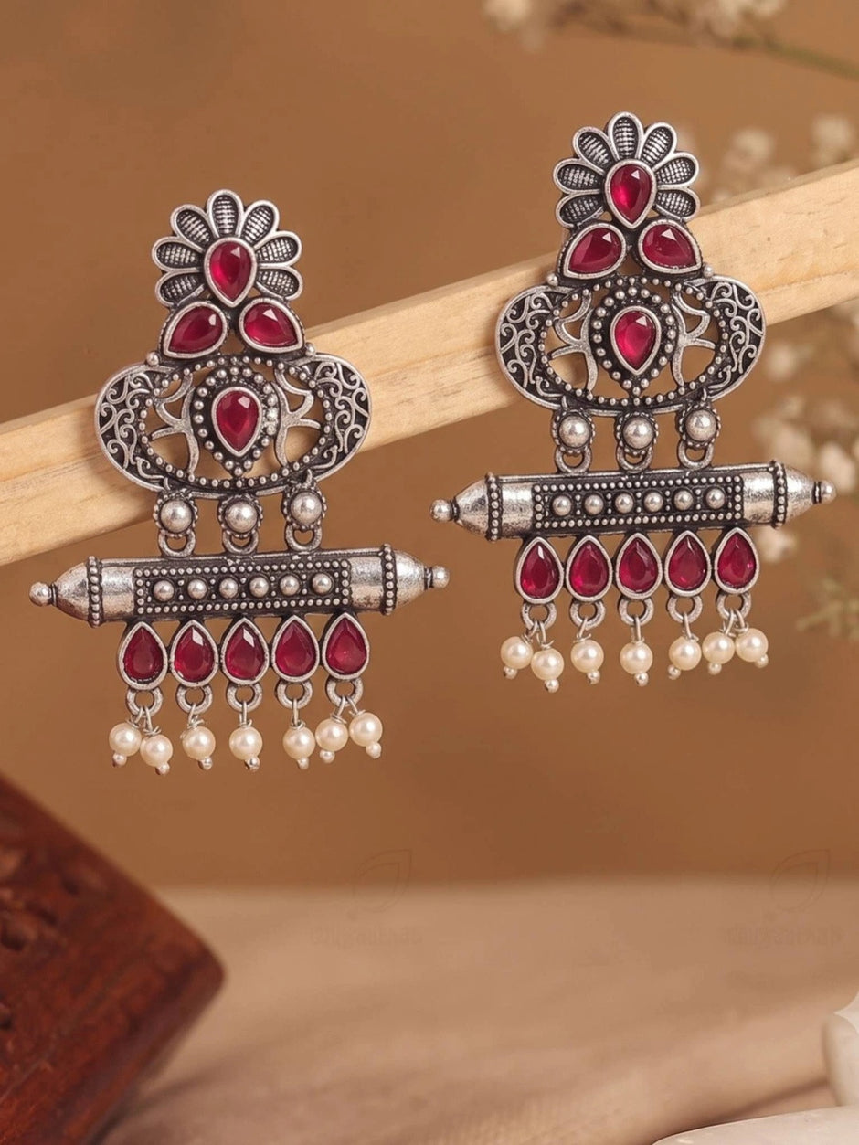 Two oxidised silver chandbali earrings balanced on wooden prop against warm beige background