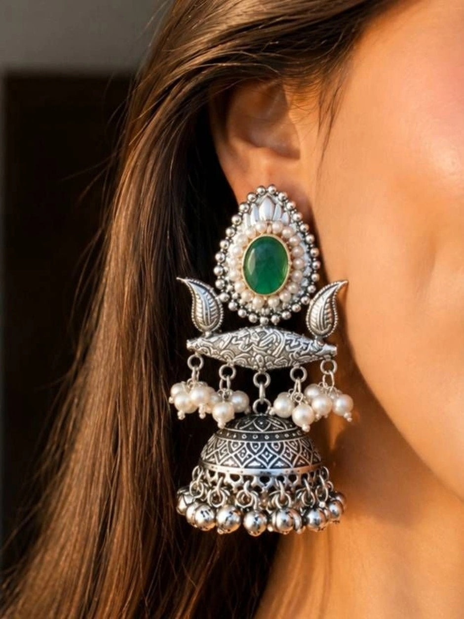 Oxidised silver teardrop jhumka earring worn on model's ear showing green stone, pearl border, leaf motifs, engraved bridge, and ghungroo bells