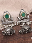 Pair of oxidised silver jhumka earrings laid flat on wooden surface showing engraved bridge, faux pearl clusters and domed bell with ghungroo