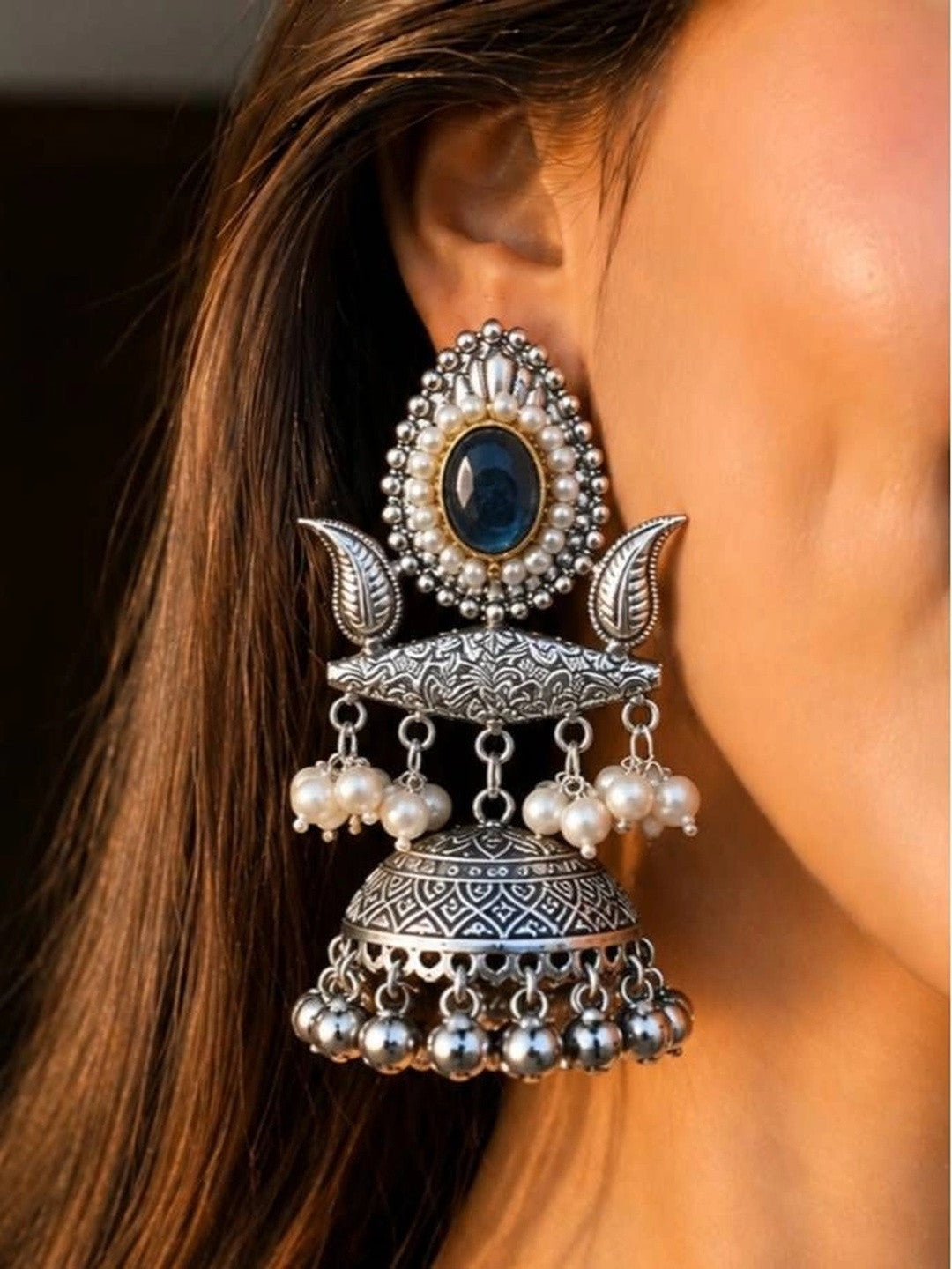 Oxidised silver jhumka earring worn on ear showing teal stone stud, pearl drops and engraved dome with ghungroo bells