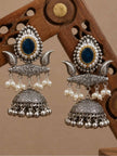 Two oxidised silver jhumka earrings leaning against carved wooden prop showing engraved dome and pearl drop bar