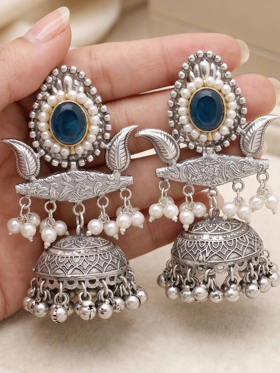 Pair of oxidised silver jhumka earrings held in palm showing full design from teal stud to ghungroo bell fringe