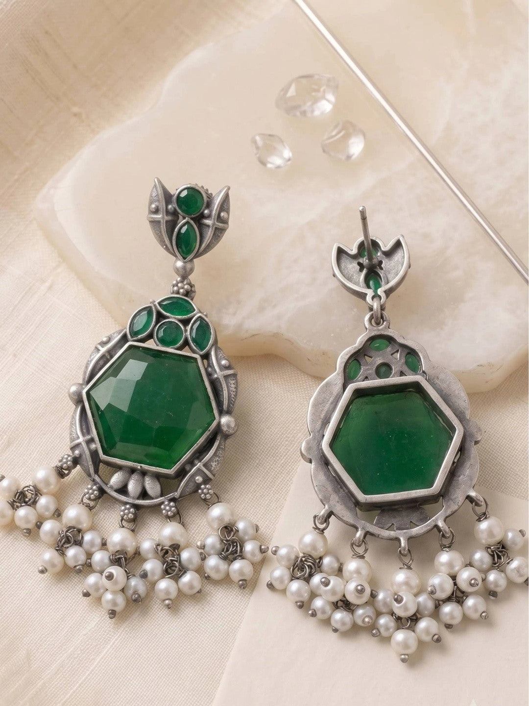Front and back view of oxidised silver green stone chandbali earrings laid flat on white surface