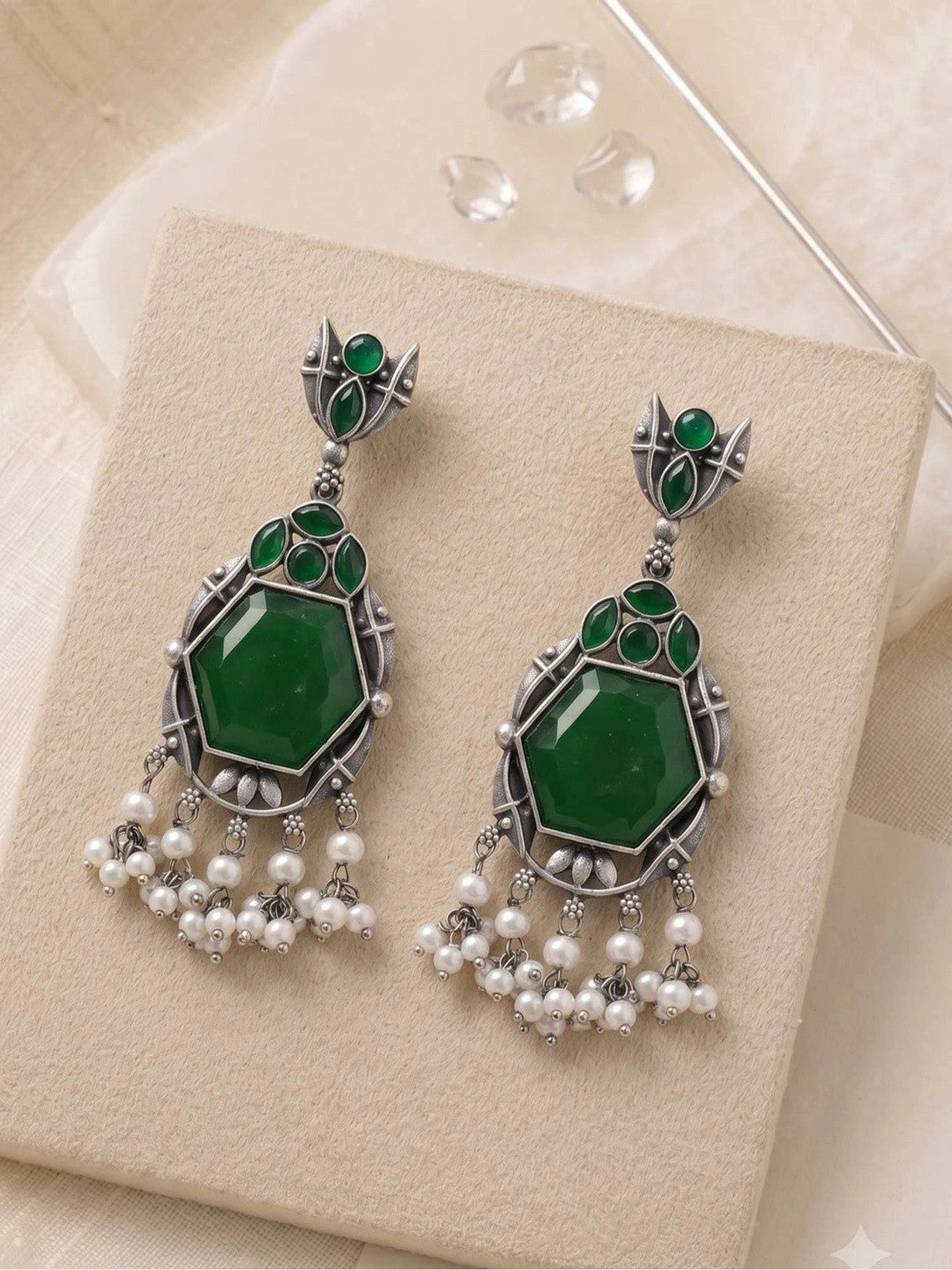 Pair of oxidised silver chandbali earrings with green stones and white pearl fringe on cream box