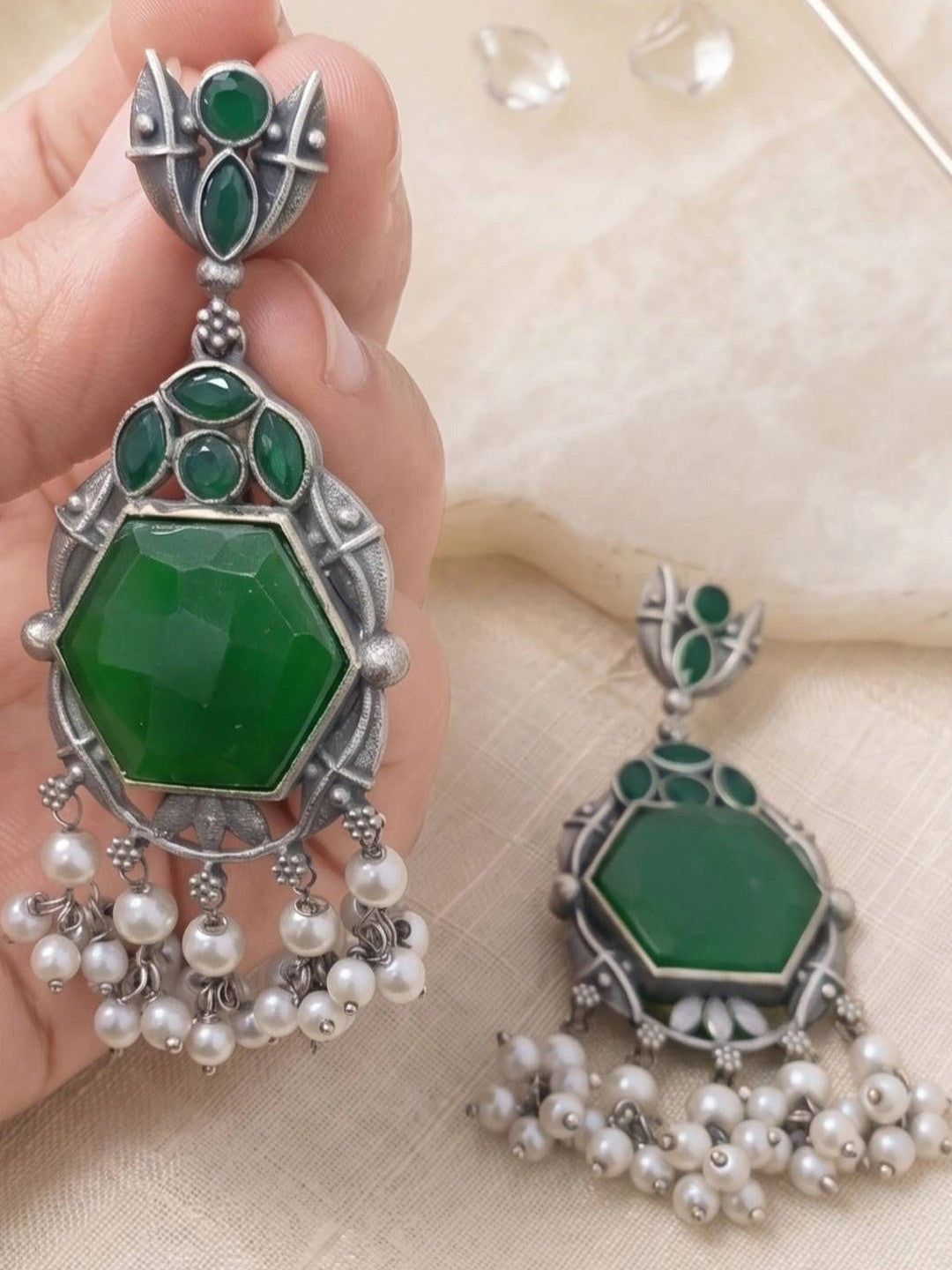 Close-up of single oxidised silver chandbali earring with faceted green stone held in hand