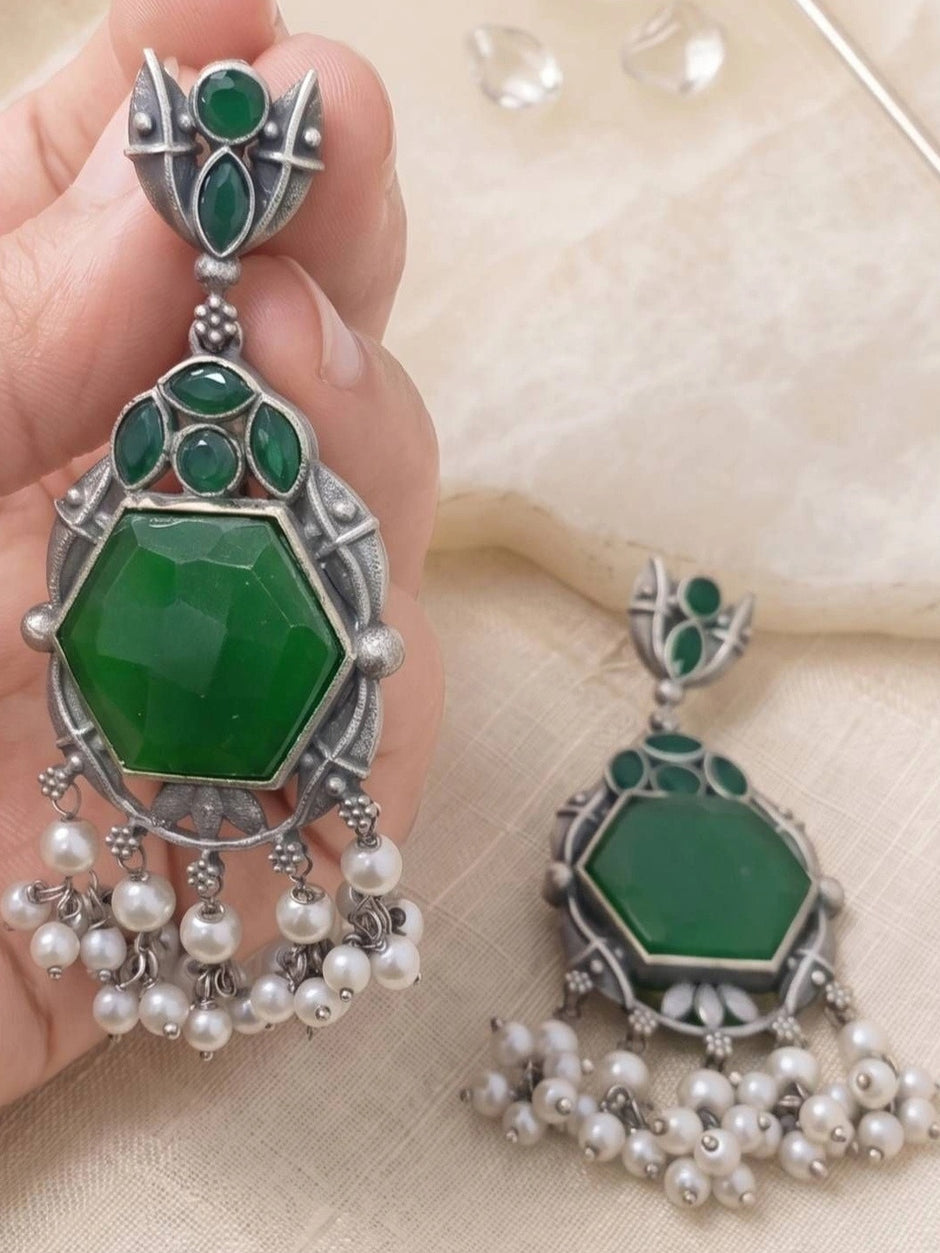 Close-up of single oxidised silver chandbali earring with faceted green stone held in hand