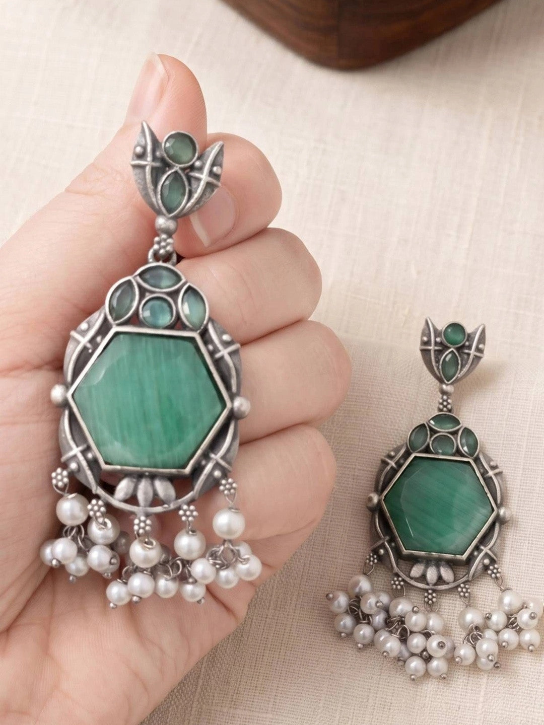One earring held in hand showing scale of green hexagon stone and pearl drop detail