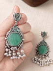 One earring held in hand showing scale of green hexagon stone and pearl drop detail