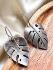 Close-up of two oxidised silver leaf earrings on a round wooden tray showing textured cut-out detail