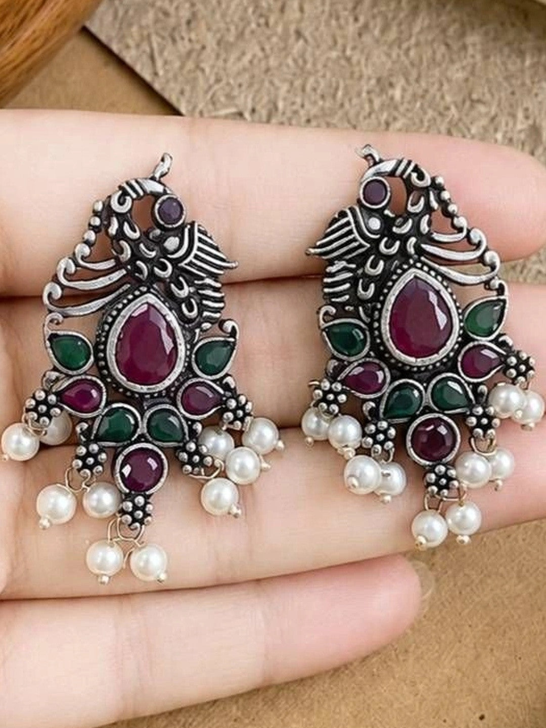 Pair of oxidised silver peacock earrings with pearl drops held in an open palm
