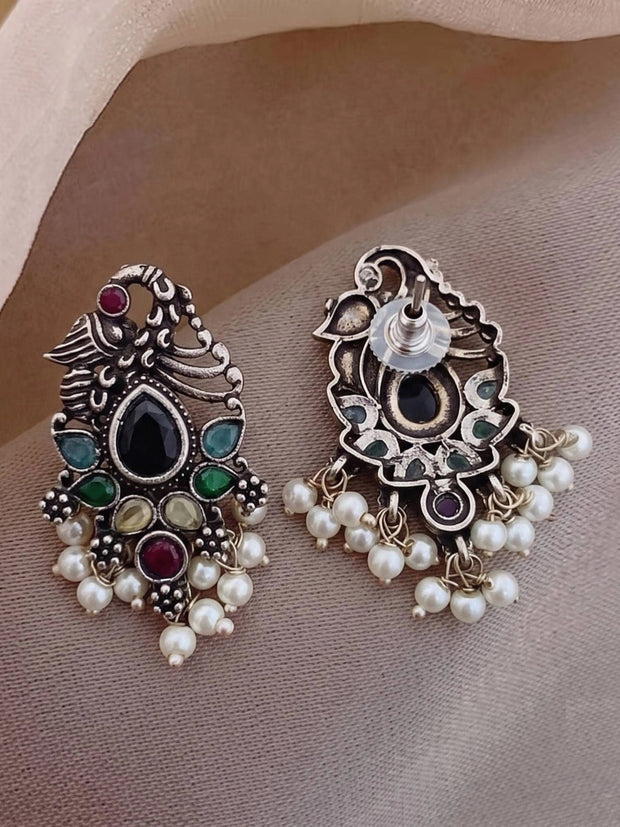 Front and back view of oxidised silver peacock earrings laid flat showing push-back stud closure and pearl drops