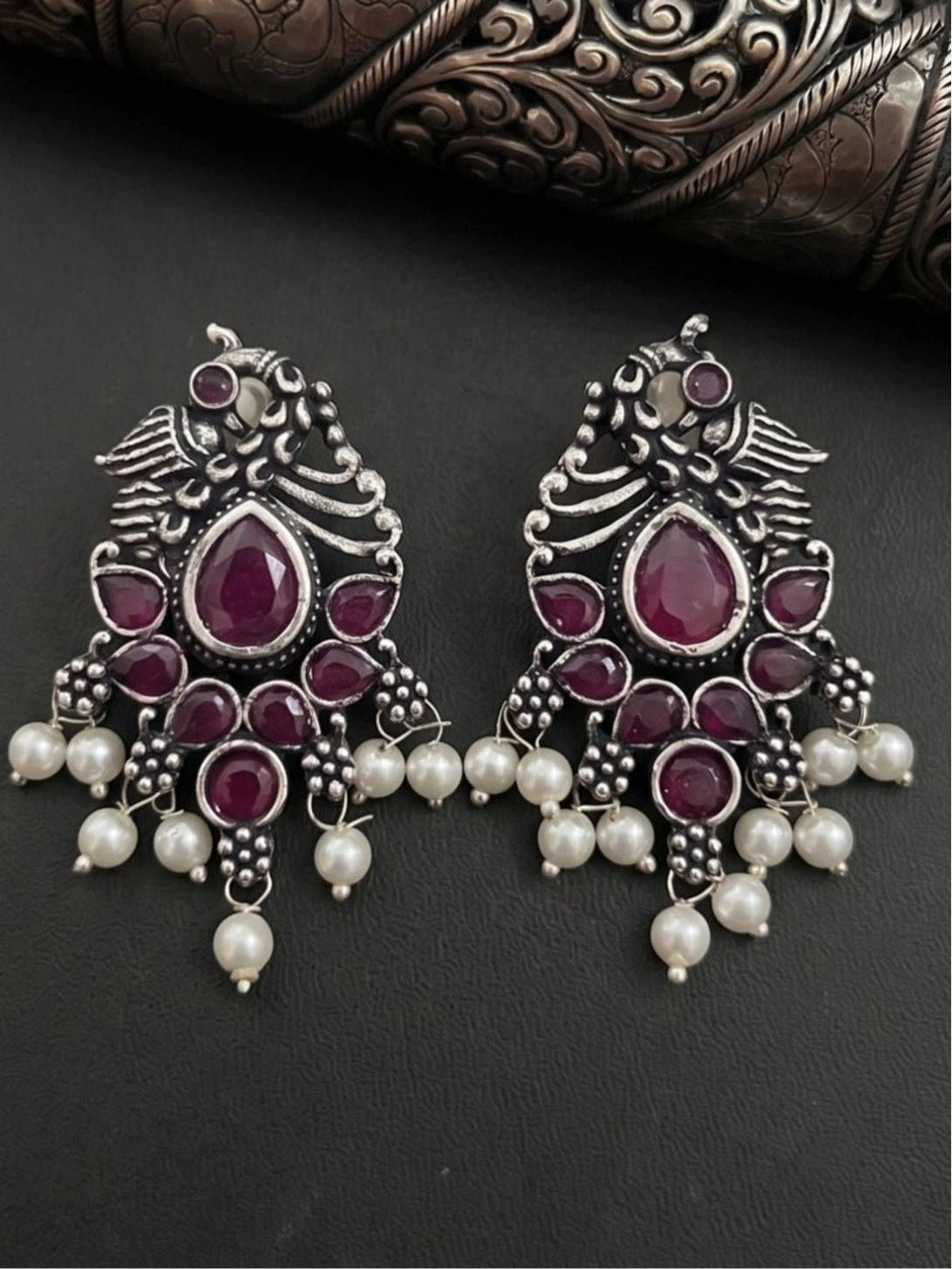Pair of oxidised silver peacock chandbali earrings laid flat on dark background