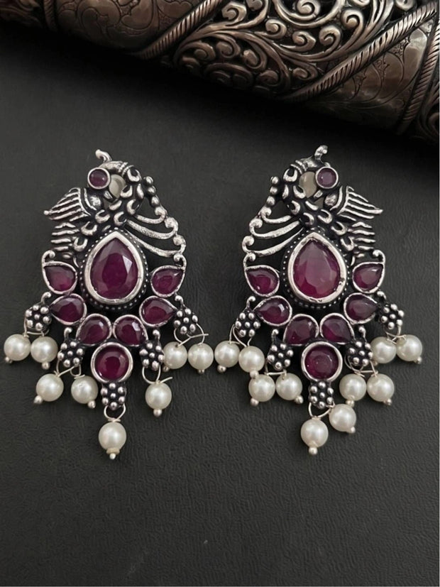 Pair of oxidised silver peacock chandbali earrings laid flat on dark background