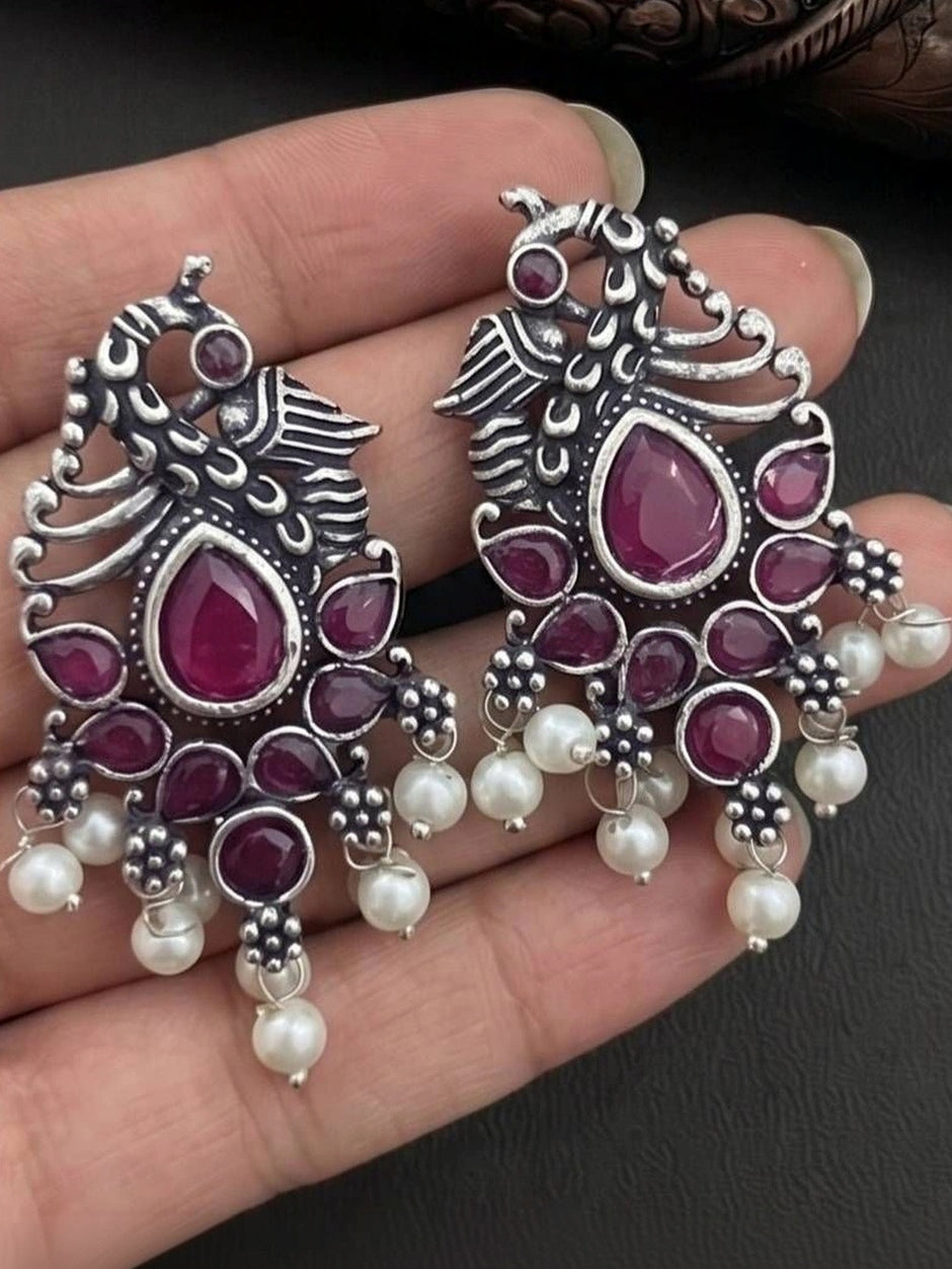 Two oxidised silver peacock earrings held in palm showing scale and full design