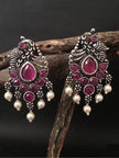 Pair of peacock chandbali earrings with pearl drops resting on a wooden branch