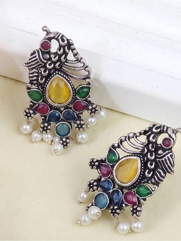 Two oxidised silver peacock earrings laid flat, front and back views, on a cream surface