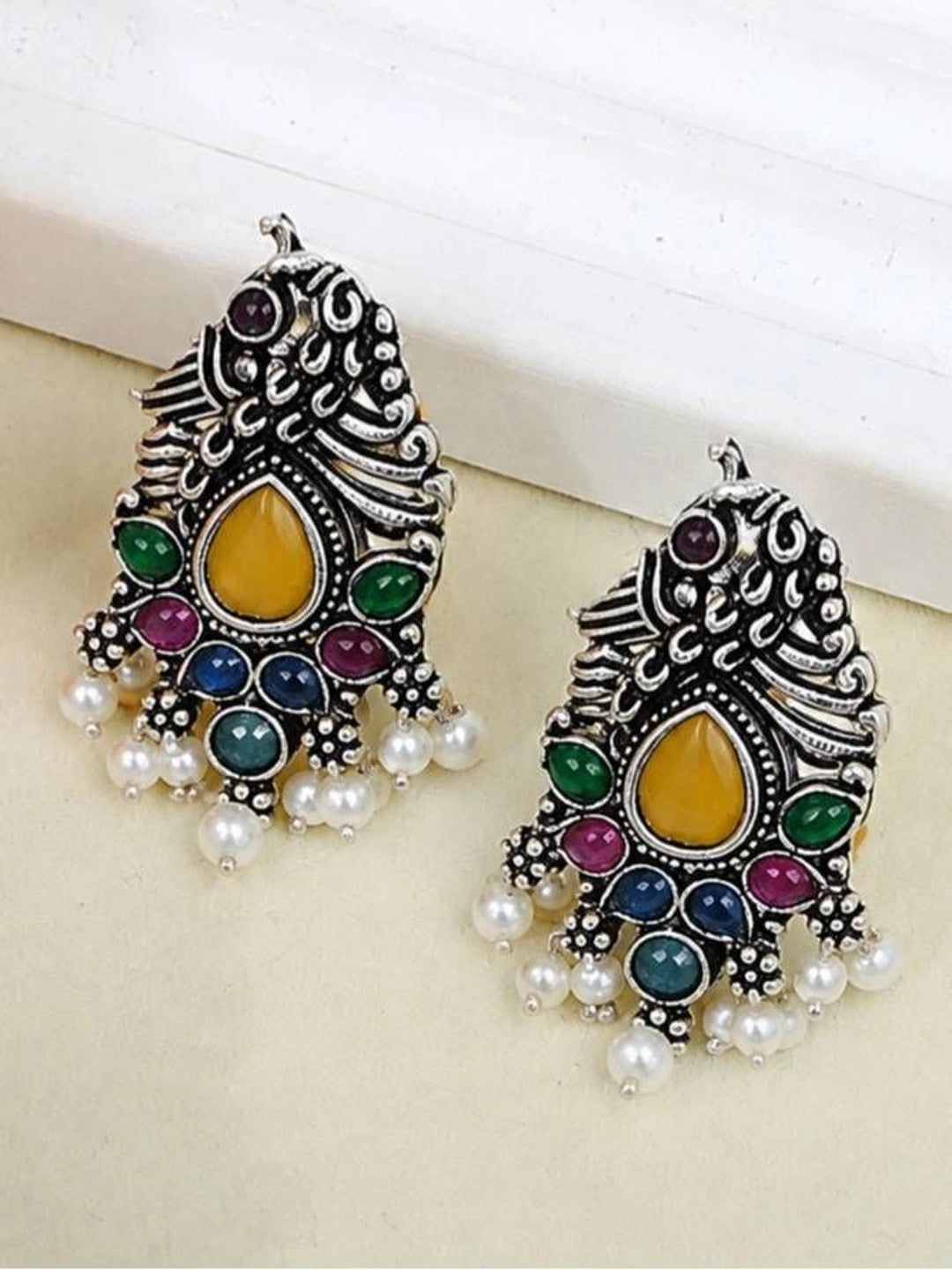 Pair of oxidised silver peacock earrings side by side showing yellow teardrop centre stone and pearl fringe