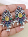 Close-up of two peacock earrings held in a hand showing coloured glass stones and pearl drops in detail