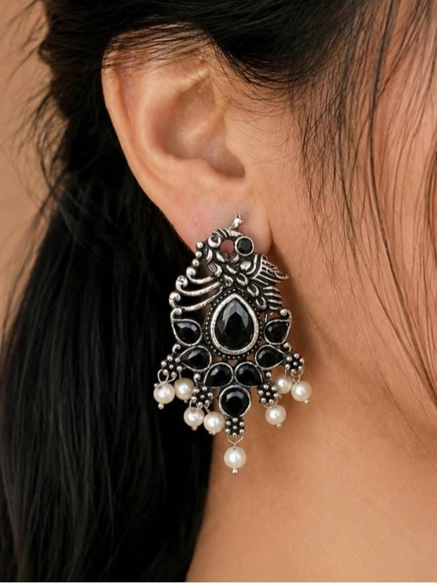 Oxidised silver peacock drop earring with black stones and pearl drops worn on ear