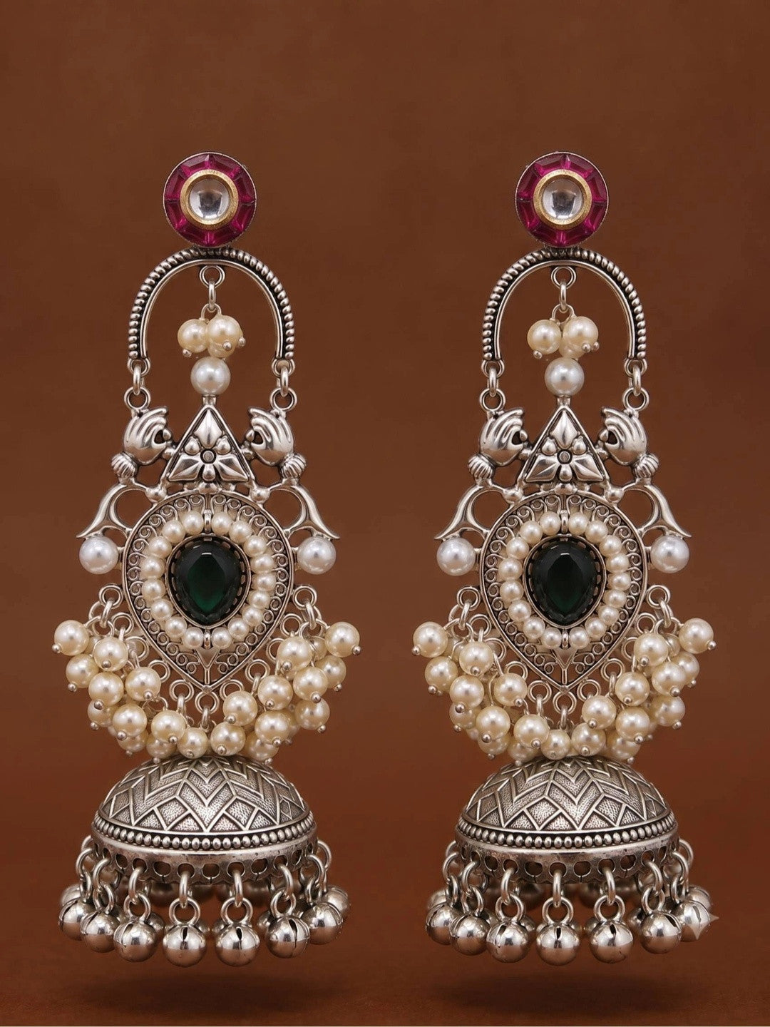 Front-facing pair of oxidised silver jhumka earrings with pink kundan tops, arched chand frame and domed ghungroo-fringed bell on brown background