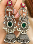 Pair of oxidised silver pearl and green stone jhumka earrings held in a woman's palm showing filigree detail and peacock motif up close