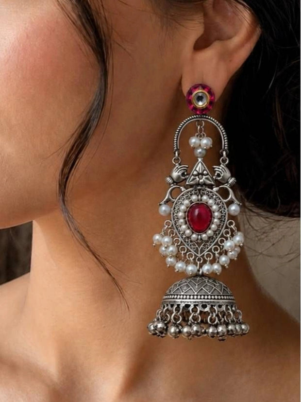 Oxidised silver jhumka earring with red stone and pearl clusters worn on a model's ear