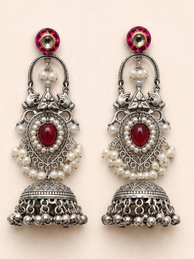 Pair of oxidised silver pearl jhumka earrings laid flat on a beige surface