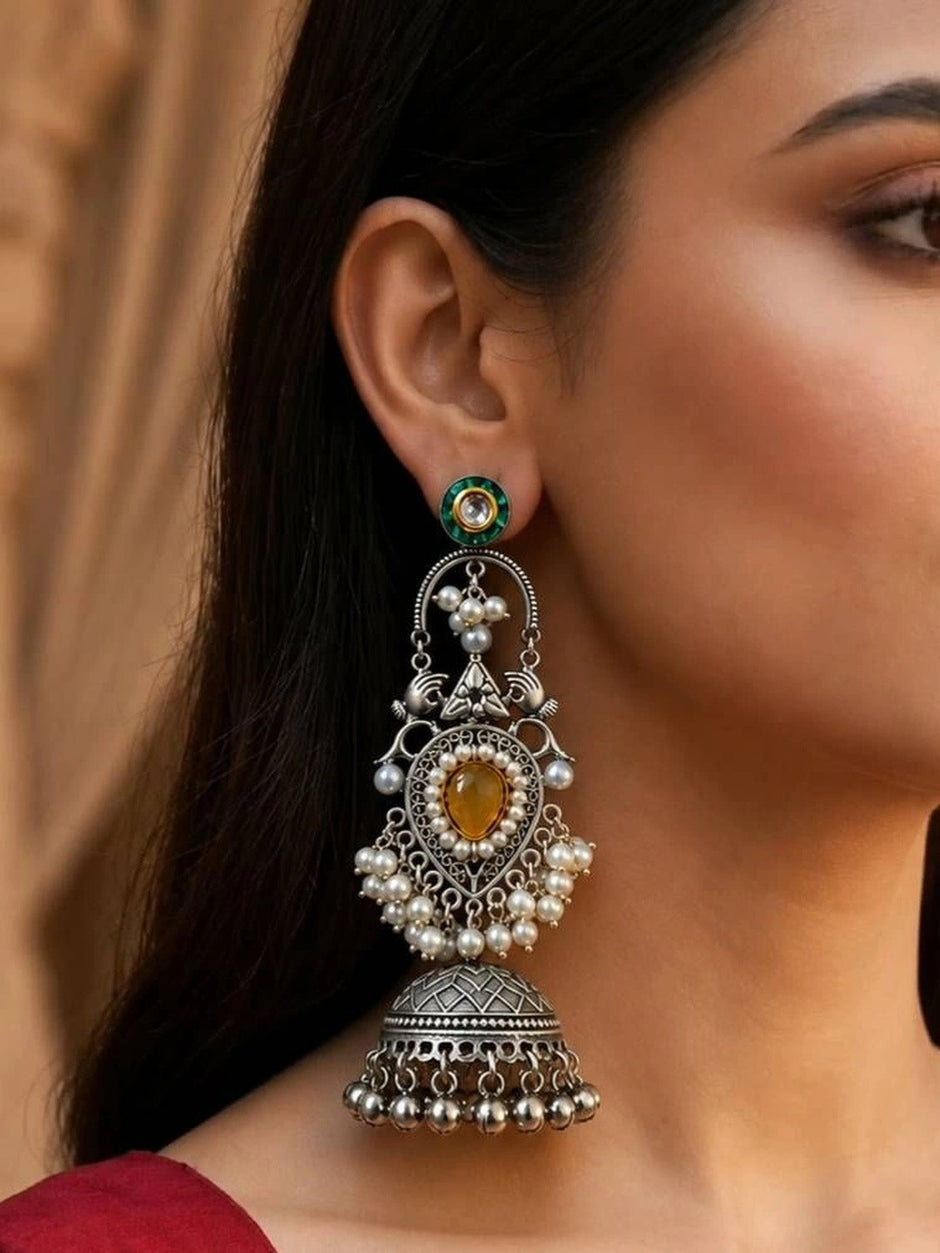 Close-up of both jhumka earrings held in a hand showing pearl detail and filigree heart pendant