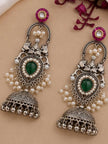 Pair of oxidised silver jhumka earrings with green stone and seed pearls laid flat on a beige surface
