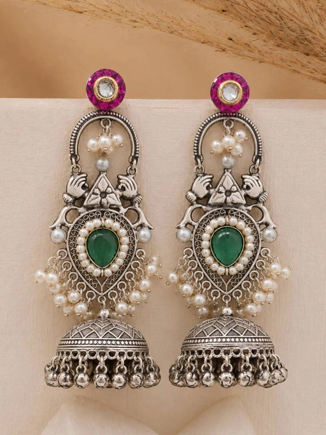 Front view of both teardrop jhumka earrings showing peacock motifs and fuchsia kundan tops on a cream background
