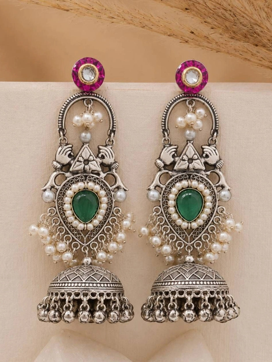 Front view of both teardrop jhumka earrings showing peacock motifs and fuchsia kundan tops on a cream background