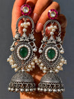Close-up of oxidised silver teardrop jhumka earring pair held in a woman's hand against a grey background