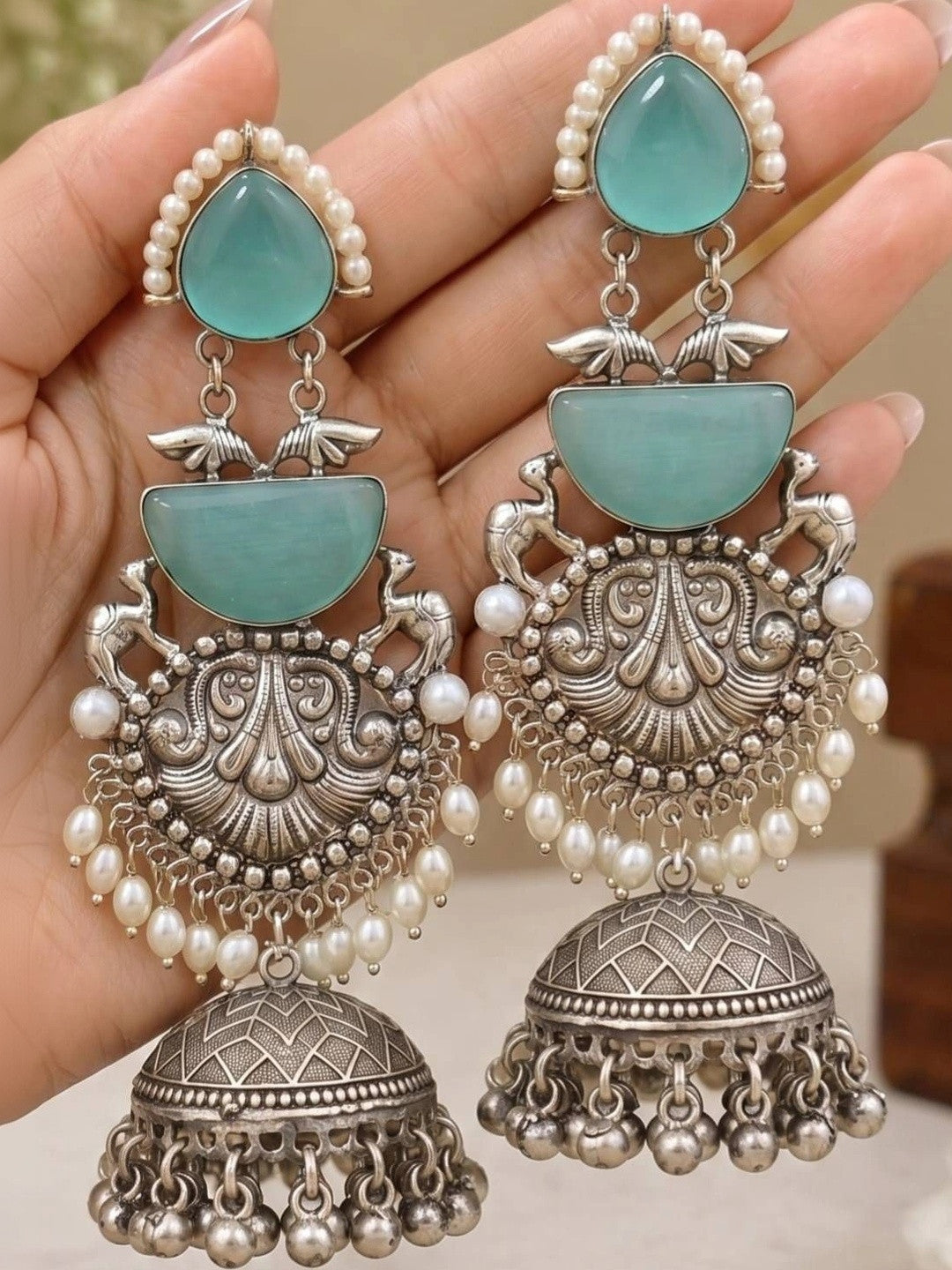 Two oxidised silver turquoise jhumka earrings held in palm showing repousse scrollwork and pearl bead drops