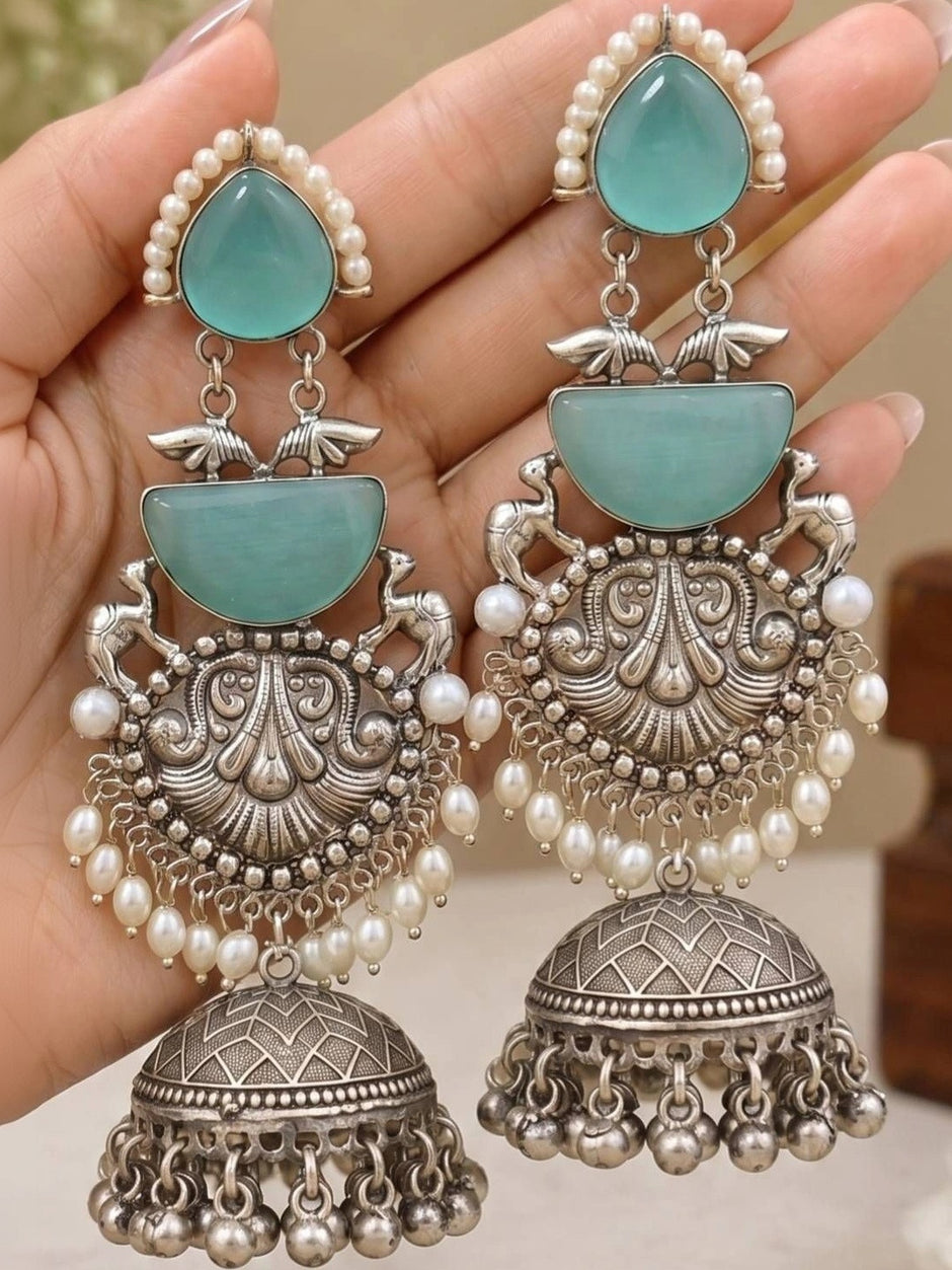 Two oxidised silver turquoise jhumka earrings held in palm showing repousse scrollwork and pearl bead drops