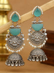 Pair of layered turquoise and oxidised silver jhumka earrings resting on wooden prop with brass vessel background