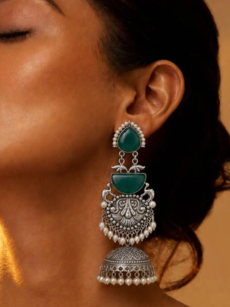Woman wearing large oxidised silver jhumka with green cabochon stones and pearl drops on ear