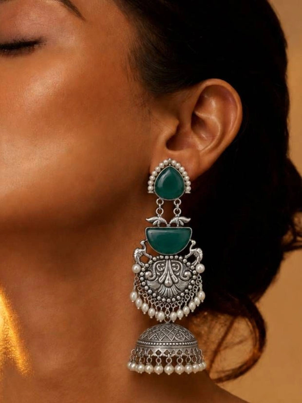 Woman wearing large oxidised silver jhumka with green cabochon stones and pearl drops on ear